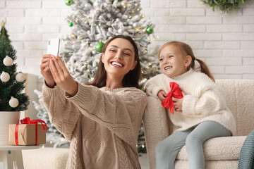 Happy young mother and her little daughter taking selfie at home on Christmas eve