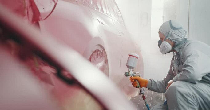 Automotive Paint Services, Quality Auto Body Shop Concept. Auto Painter Spraying Red Paint on Car Door in Special Booth. Painting Vehicle Parts at Car Service Workshop. Car Manufacturing Factory
