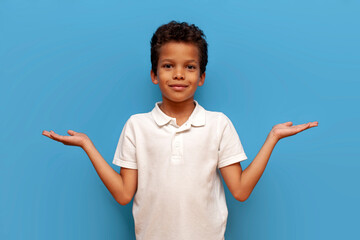 curly african american boy in white t-shirt holds empty hands on yellow isolated background