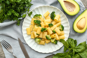 Plate of tasty pasta with broccoli and avocado on grey background