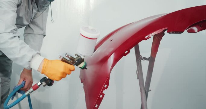 Painting Vehicle Parts at Car Service Workshop. Car Manufacturing Factory. Automotive Paint Services, Quality Auto Body Shop Concept. Auto Painter Spraying Red Paint on Car Door in Special Booth