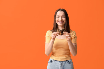 Beautiful young woman with tasty cookie on orange background