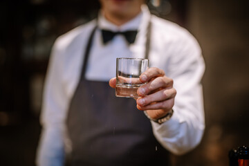 hands of a male bartender accurate holding clean transparent empty glass for booze. Blurred bar background
