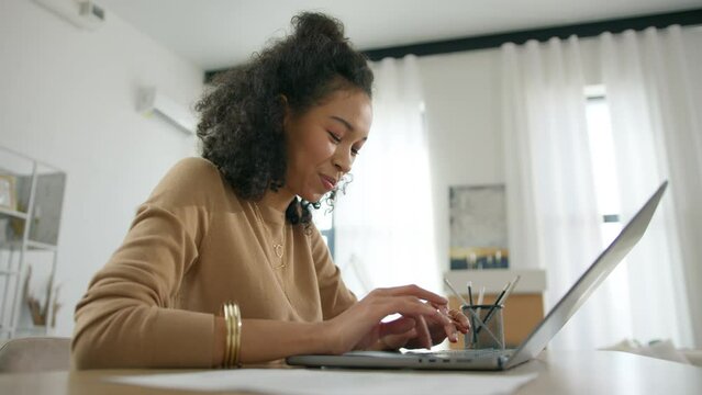 Productive positive businesswoman sitting at desk working on laptop computer. Woman working with big data e-commerce analysis. Smiling multi ethnical woman at work. Remote work in home office dolly 4K