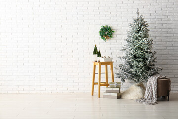 Beautiful Christmas tree with gift boxes and ottoman near white brick wall