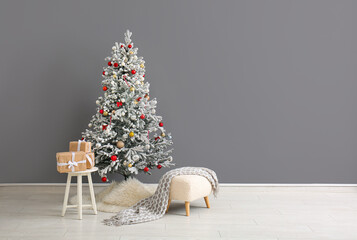 Beautiful Christmas tree with gift boxes and ottoman near grey wall