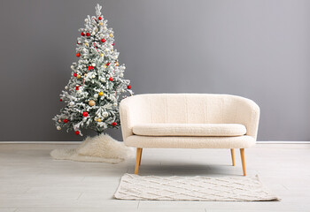 Beautiful Christmas tree with comfortable sofa near grey wall