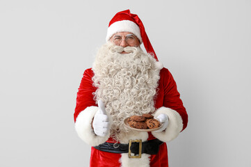 Fototapeta na wymiar Santa Claus with plate of tasty cookies showing thumb-up on white background