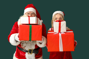 Santa Claus and beautiful woman with Christmas gifts on green background