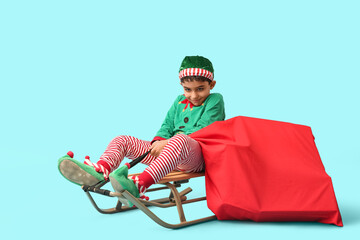 Cute little elf with sled and bag of gifts on blue background