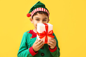 Cute little elf with Christmas gift on yellow background