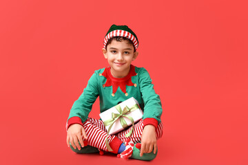 Cute little elf with Christmas gift on red background