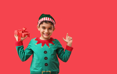 Cute little elf with Christmas gift pointing at something on red background