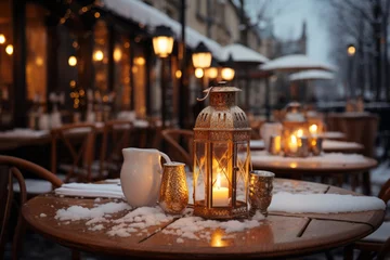 Deurstickers Lit lantern as a decoration of a wooden restaurant table on Christmas time. Decorated and illuminated outdoor tables of a restaurant of cafe in France. Snowy winter day. © MNStudio