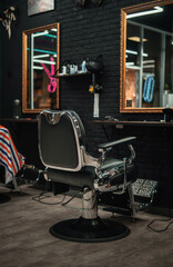 Stylish black leather barber chair in front of the mirror in the dark interior of the hairdressing...
