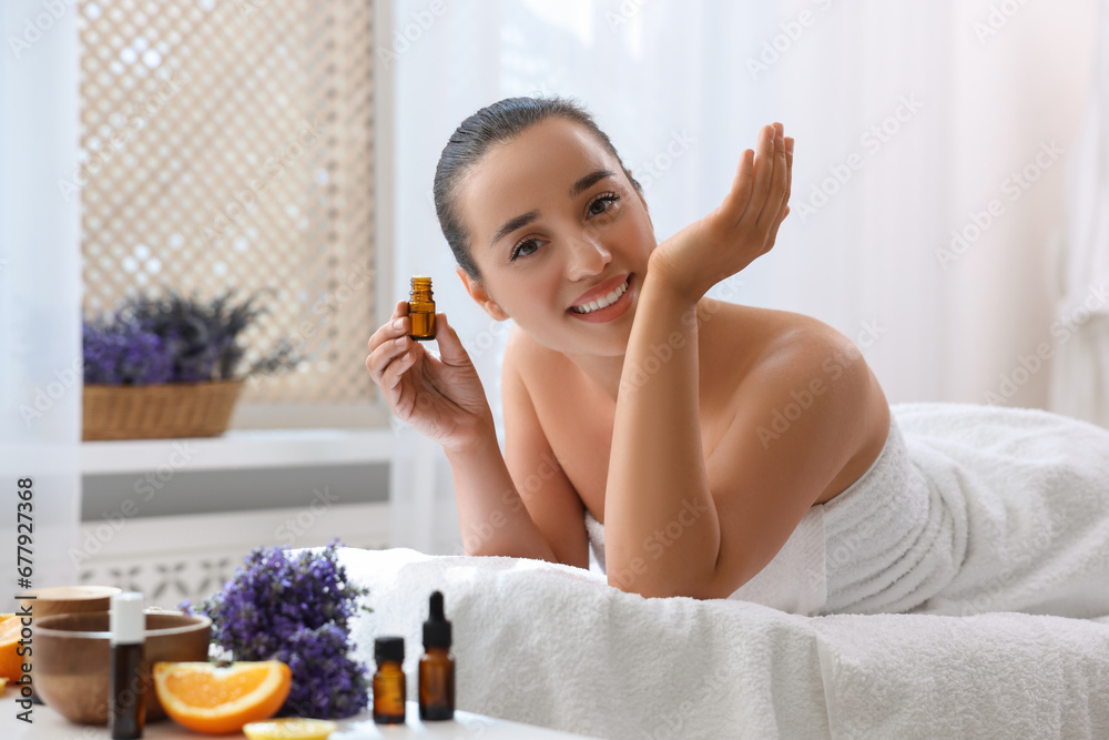 Poster Happy young woman with bottle of essential oil in spa salon