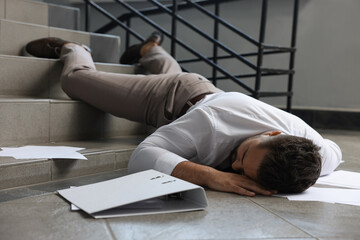 Unconscious man with scattered folder and papers lying on floor after falling down stairs indoors - obrazy, fototapety, plakaty