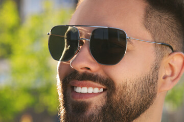 Handsome smiling man in sunglasses outdoors, closeup. Space for text