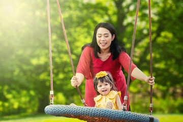 Mother playing with her daughter on a swing in the park