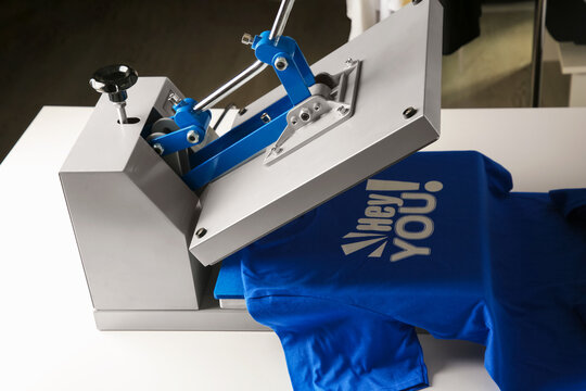 Printing logo. Heat press with blue t-shirt on white table