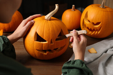 Woman carving pumpkin for Halloween at wooden table, closeup