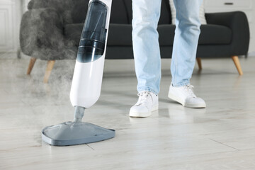 Fototapeta na wymiar Man cleaning floor with steam mop at home, closeup