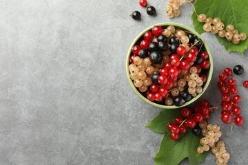 Different fresh ripe currants and green leaves on light grey table, flat lay. Space for text