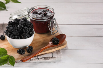 Fresh ripe blackberries, tasty jam and leaves on white wooden table. Space for text