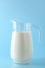 Jug of fresh milk on light blue background