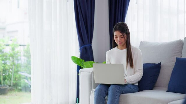 Young asian woman using laptop while seated on couch at home