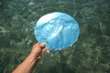 Woman immersing round mirror in sea on sunny day, above view