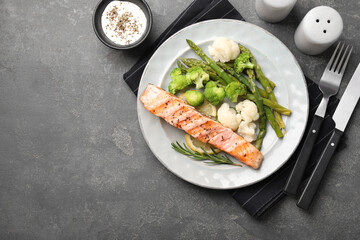 Healthy meal. Piece of grilled salmon, vegetables, asparagus and rosemary served with sauce on grey textured table, flat lay. Space for text