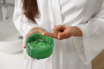 Young woman holding jar of aloe hair mask indoors, closeup