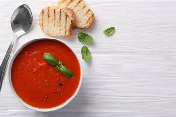 Delicious tomato cream soup in bowl served with pieces of grilled bread on white wooden table, flat...