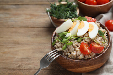 Tasty boiled oatmeal with egg, tomatoes and microgreens served on wooden table, space for text