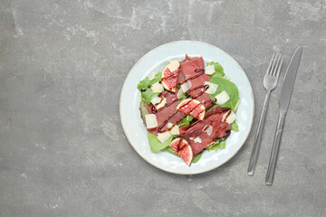 Plate with delicious bresaola salad served on grey textured table, flat lay. Space for text