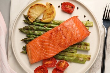Tasty grilled salmon with asparagus, tomatoes, spices and lemon served on light grey table, top view