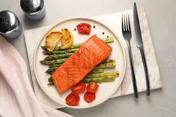 Tasty grilled salmon with asparagus, tomatoes, spices and lemon served on light grey table, top view