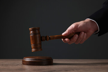 Judge with gavel at wooden table against black background, closeup - obrazy, fototapety, plakaty