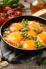 Delicious Shakshuka in frying pan on wooden table, closeup