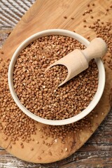 Bowl and scoop with dry buckwheat on wooden table, top view
