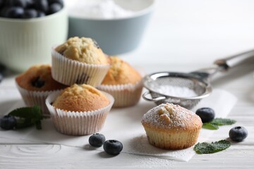 Delicious sweet muffins powdered with sugar, blueberries and mint on white wooden table, closeup
