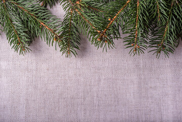 Natural spruce coniferous green branches with two white candles in candlesticks in the form of cones on a grey linen tablecloth background. Festive decoration of the Christmas table. Top view.