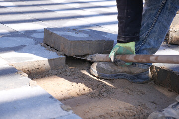 Worker remove large concrete blocks on a sandy surface. 