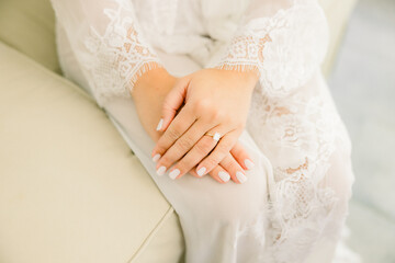 Obraz na płótnie Canvas Bride is sitting in a lace robe on her wedding day with her hands in her lap, showing off her engagement ring