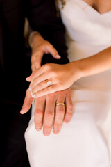 Bride and groom are sitting together with their hands together showing off their wedding bands. 