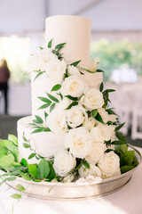 A beautiful three-tiered wedding cake decorated with white roses and greenery. 
