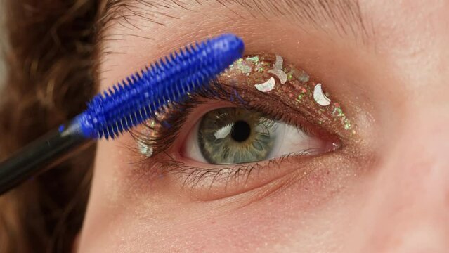 Blue mascada makeup to the upper lashes, close-up. Makeup artist applies a bright glitter eyeshadow with a makeup brush.Tutorial master class of professional makeup. 