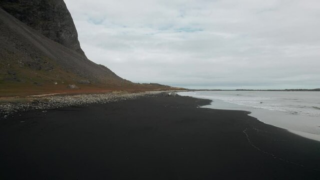Aerial flying along black sand beach stokksnes, volcanic dark mountains in distance, dark moody cloudy scenery Iceland