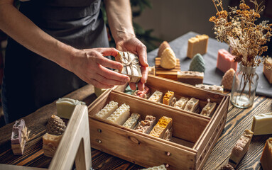 A woman soap maker holds handmade soap in her hands. A lot of different sliced pieces in a wooden box. Eco-friendly natural handmade cosmetics